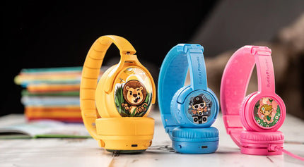 Colorful children's BuddyPhones (headphones) in yellow, blue, and pink, featuring fun cartoon stickers and soft cushions, displayed with books.