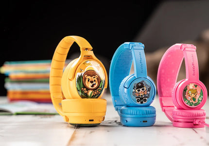 Colorful children's BuddyPhones (headphones) in yellow, blue, and pink, featuring fun cartoon stickers and soft cushions, displayed with books.