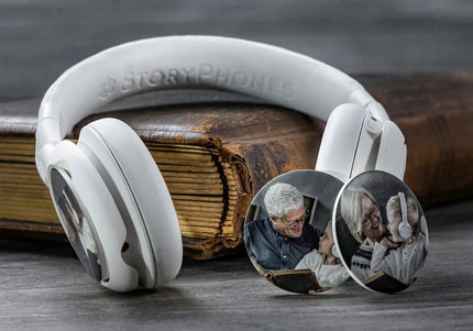 A pair of Onanoff white StoryPhones (headphones) rests on a vintage book, showcasing circular StoryShields customized with family photos.