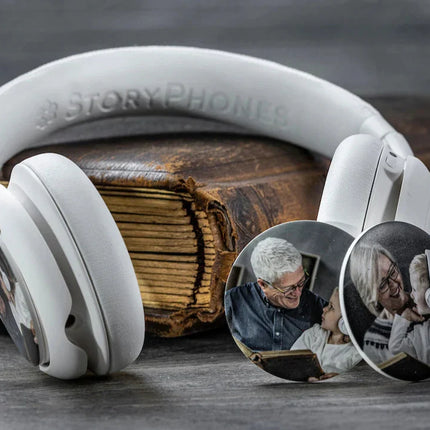 A pair of Onanoff white StoryPhones (headphones) rests on a vintage book, showcasing circular StoryShields customized with family photos.