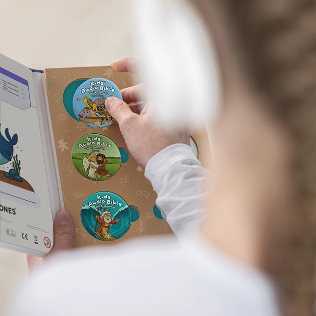 Child in a white shirt holds the ONANOFF Bible Stories Old Testament open, revealing Kids' Audio Bible StoryShields with biblical illustrations. 